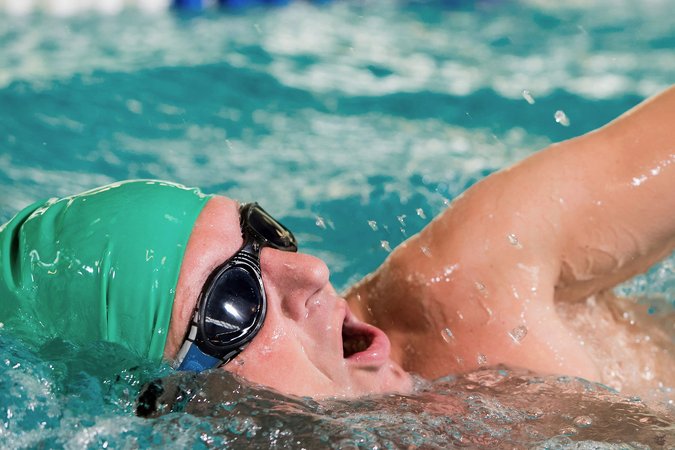 Ein Schwimmer mit Schwimmbrille und Schwimmhaube schwimmt im Kraulen durch ein Becken.